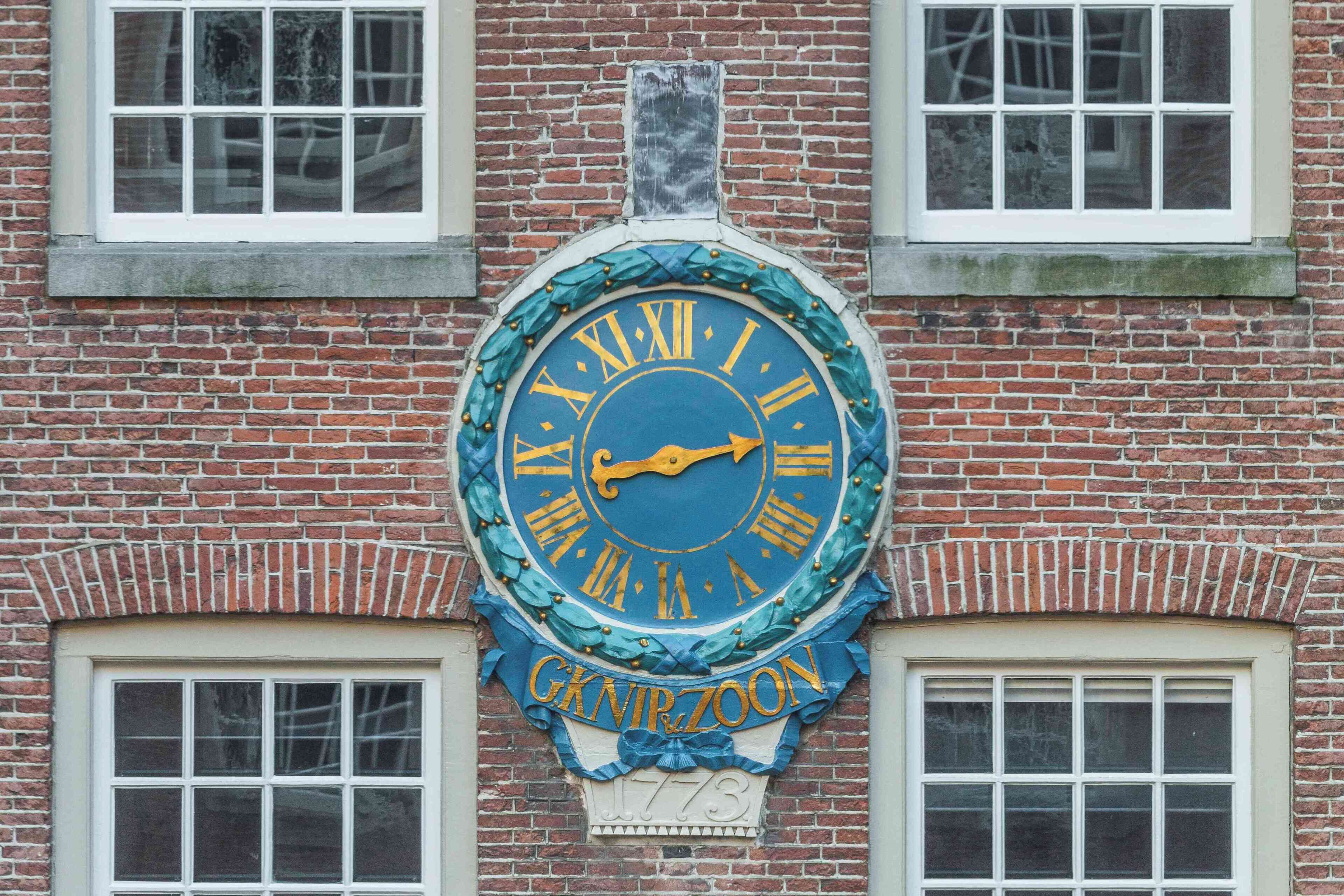 Een klok met Romeinse cijfers en het jaartal 1773 op een bakstenen gebouw.