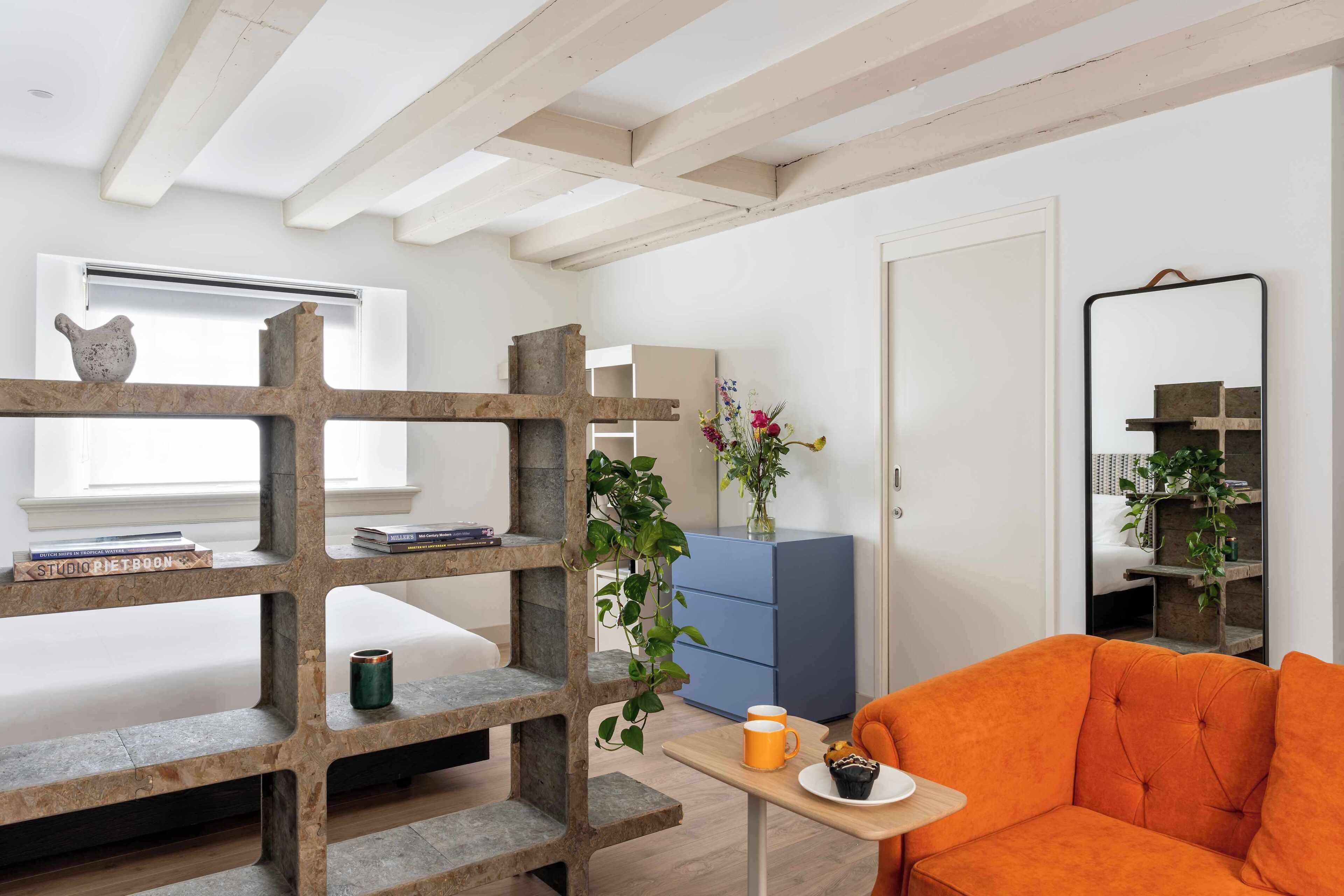 A room with a wooden bookshelf, a sofa, a small table with a cup, and a mirror on the wall.
