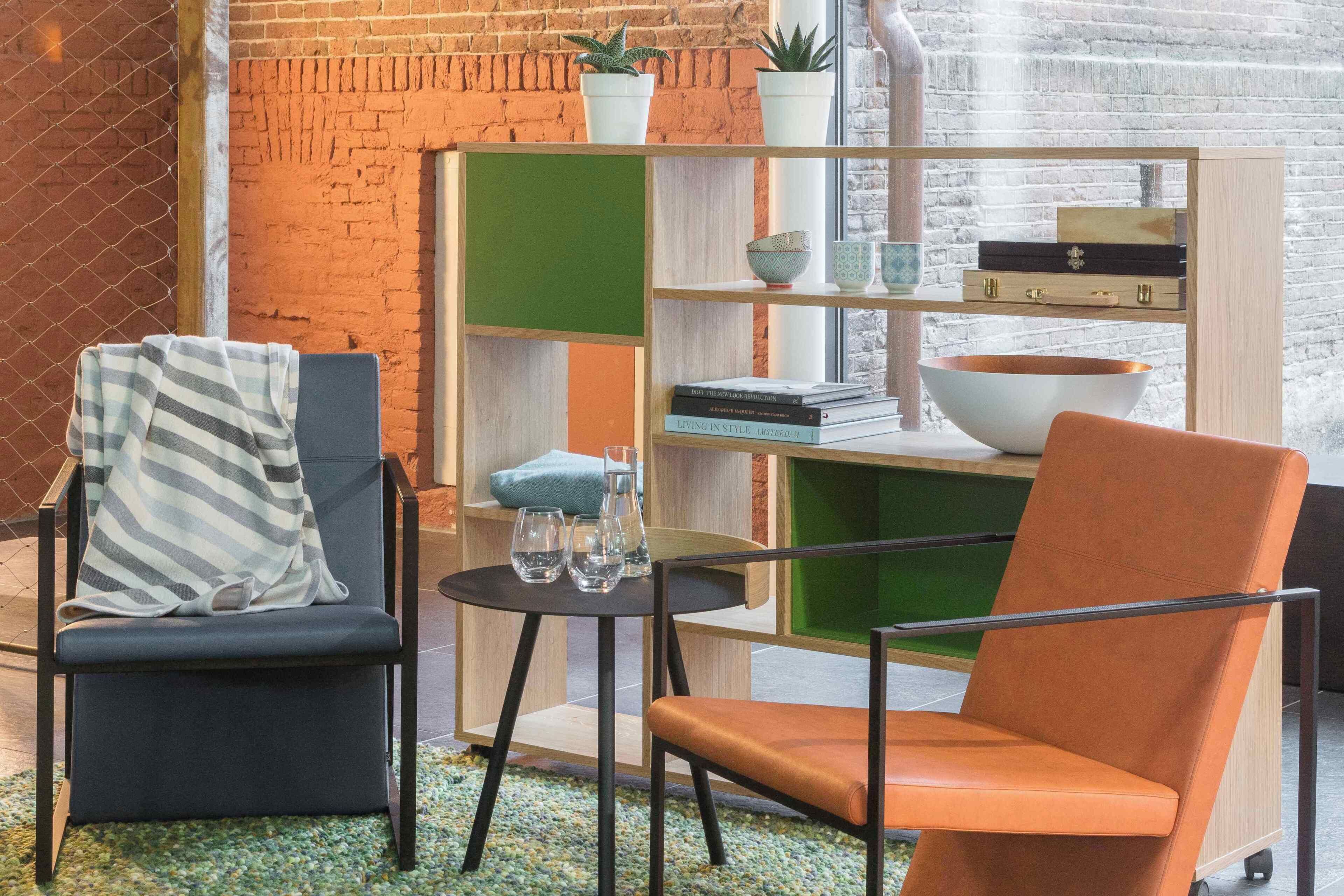 A room with two chairs, a small table, a bookshelf, and a window with a brick wall.