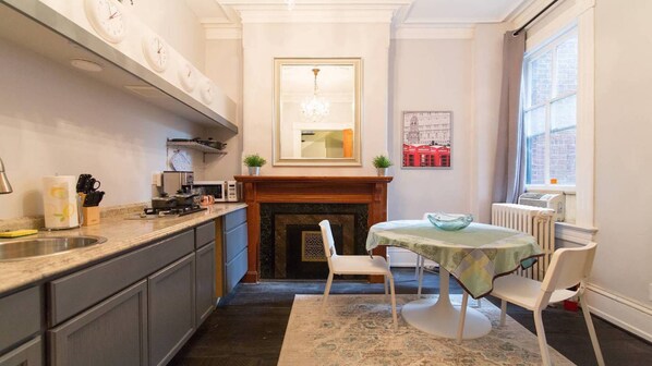 Una cocina compacta con chimenea central, un comedor con mesa y sillas, y un ventanal que proporciona luz natural.