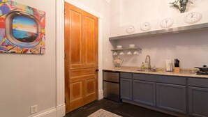 Une cuisine avec une porte en bois, un tableau abstrait aux couleurs vives, une horloge et un évier.