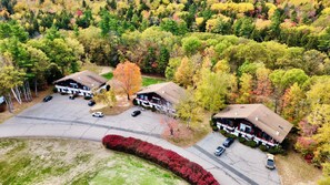 Vue aérienne d’un chalet composé de deux bâtiments principaux, d’un espace de stationnement et de la forêt environnante.