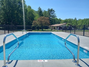 A rectangular swimming pool with metal handrails, surrounded by a black fence, trees, and a building in the background. - Walk to StoryLand! Updated Condo! WiFi/Golf/AC/Pool - New Pool 2026 (Glen)