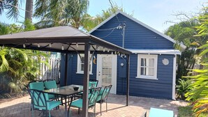 A blue house with a covered patio, a table with chairs, and a garden with palm trees. -  BEAUTIFUL PRIVATE COTTAGE   (Lake Worth)