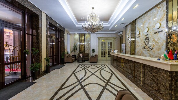 A hotel lobby with a marble floor, a chandelier, seating area, and a reception desk with flags. - The Plaza Hotel (Almaty)