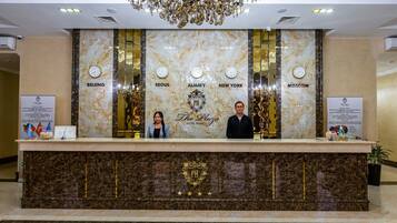 A hotel reception desk with a marble counter and a chandelier above.