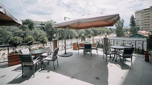 An outdoor patio with round tables and chairs, covered by large umbrellas, and surrounded by a decorative fence. - The Plaza Hotel (Almaty)