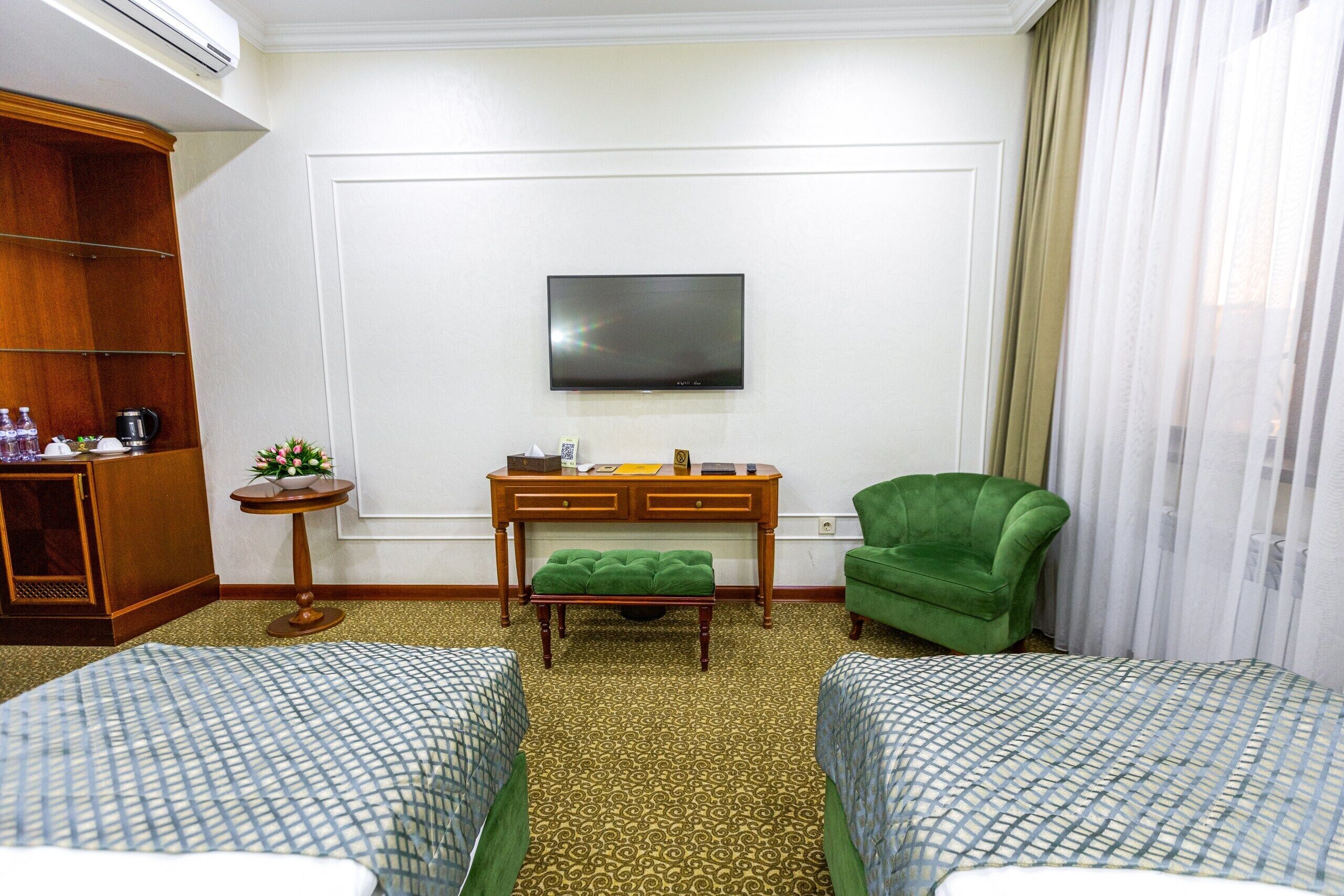 Habitación de hotel con dos camas, un televisor montado en la pared, un escritorio con una silla y un sillón verde.
