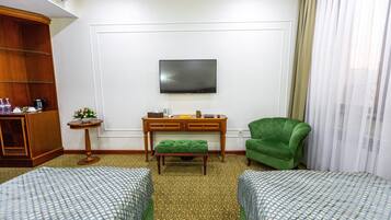 Habitación de hotel con dos camas, un televisor montado en la pared, un escritorio con una silla y un sillón verde.