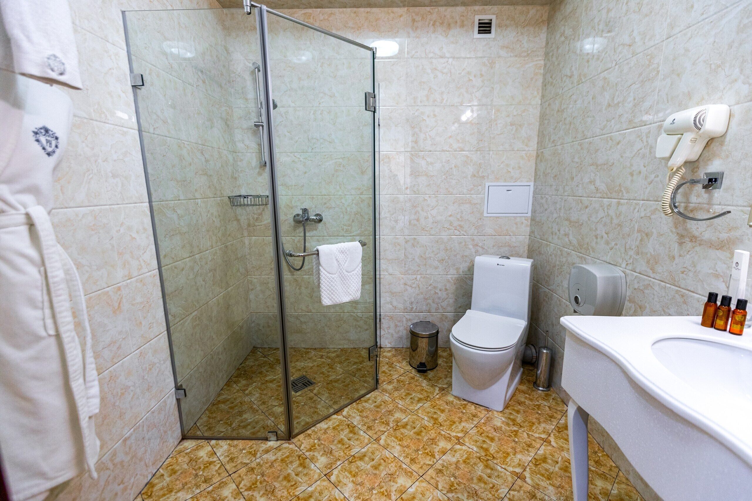 Un baño con ducha envuelta en vidrio, inodoro y lavamanos con artículos de aseo.