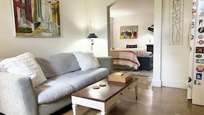 Una sala de estar con un sofá gris, una mesa de centro de madera y un cuadro que muestra una escena callejera.