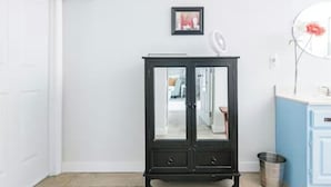 Una habitación con un mueble negro, una puerta blanca, un mueble azul, un ventilador y un cubo de basura.
