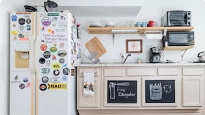 Una cocina con un refrigerador lleno de calcomanías, un microondas, un tostador y una pizarra con la frase 'Extintor' escrita.