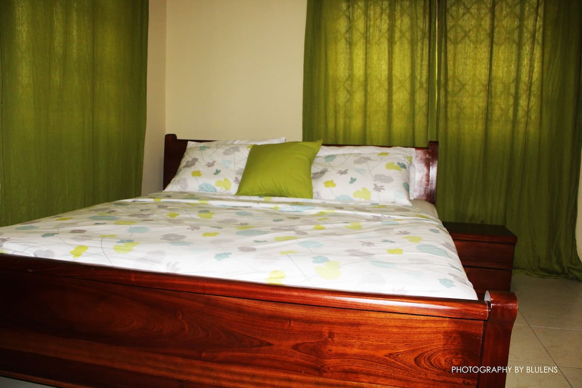 A wooden bed with a floral bedspread and green pillows in a room with green curtains.