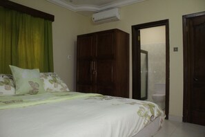 Un dormitorio con cama, armario, puerta de baño y equipo de aire acondicionado.