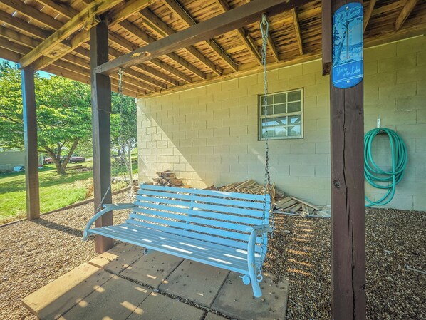 A covered outdoor seating area with a bench, a hanging chain, a window, and a hose.