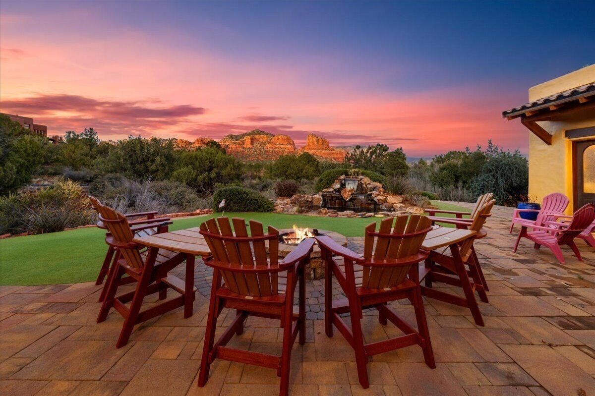 Eine Terrasse mit Holzstühlen und einem Tisch, einer Feuerstelle und Blick auf eine gebirgige Landschaft bei Sonnenuntergang.