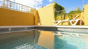 Una piscina con agua cristalina, una silla de descanso blanca y una pared amarilla.