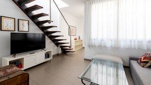 Una sala de estar moderna con una escalera, un televisor de pantalla plana, una mesa de centro de vidrio y un sofá.