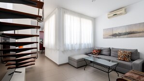 Un salón moderno con un sofá gris, una mesa de centro de vidrio y una escalera con barandillas de madera.