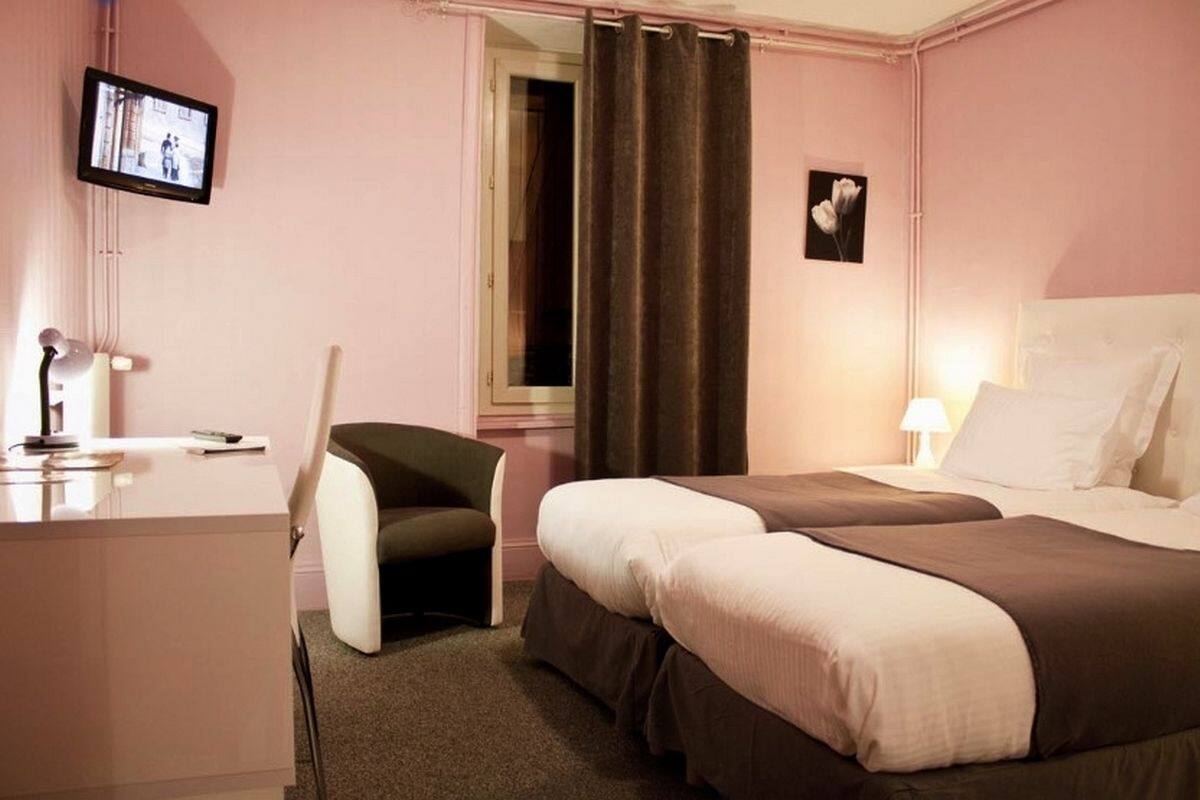 A hotel room with a bed, bedside table, lamp, chair, desk, TV, and curtains.