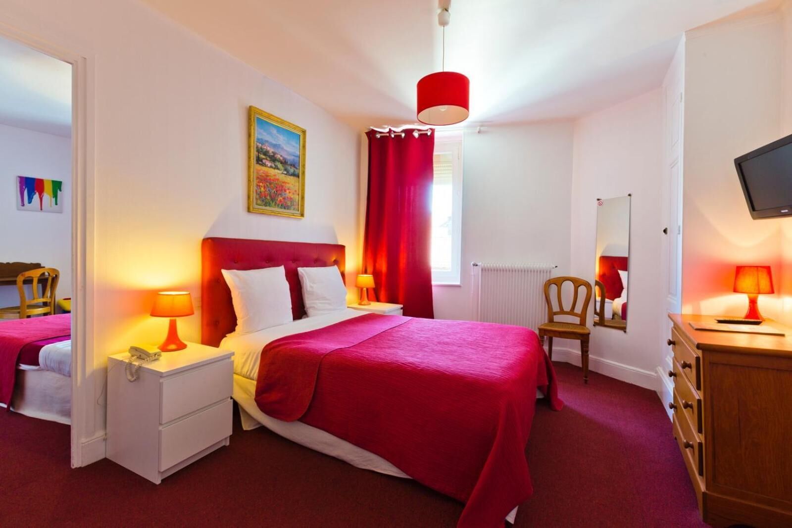 A hotel room with a bed, a nightstand, a chair, a dresser, a television, and a window with red curtains.