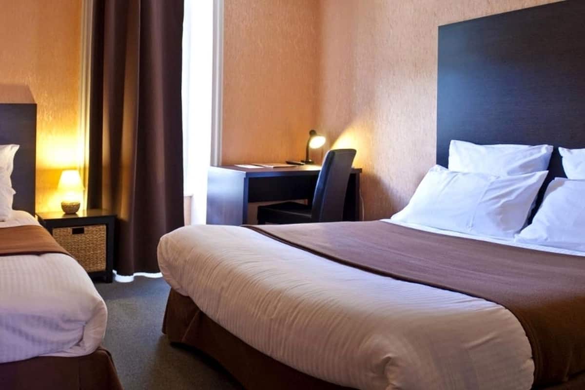 A hotel room with two beds, a desk, and a chair.