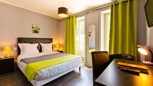 A hotel room with a bed, bedside tables, a desk, a chair, a desk lamp, and a TV. - Hôtel de la Poste (Pontgibaud)