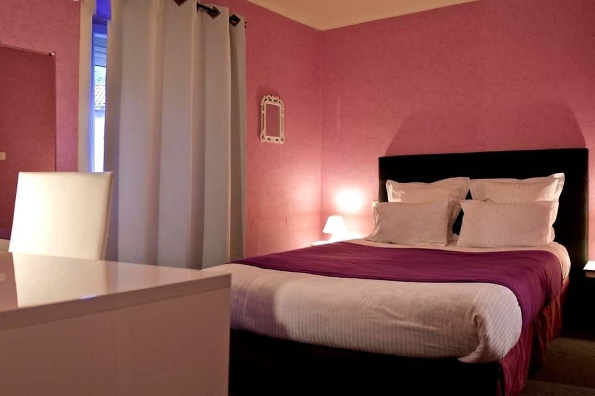 A bedroom with a bed, two bedside lamps, a nightstand, a mirror, and a window with curtains.