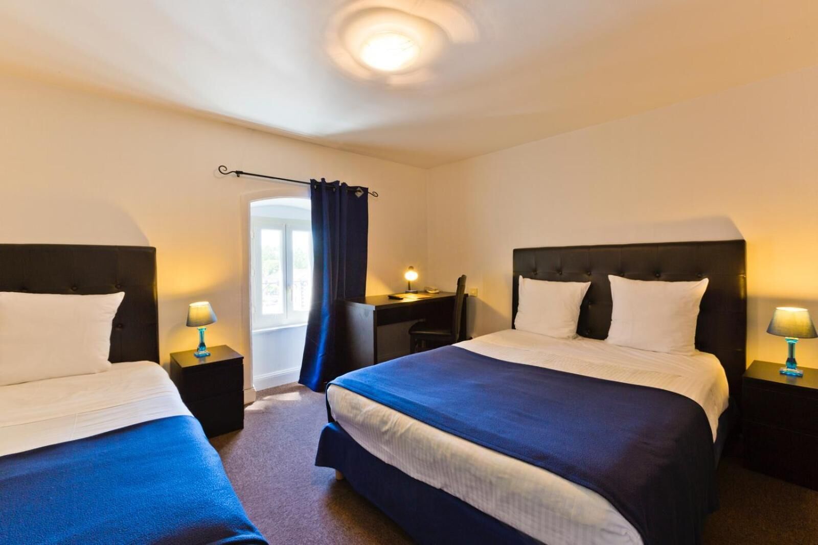 A hotel room with two beds, a desk, a chair, and a window with curtains.