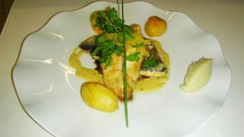 Un plato blanco con un filete de pescado, patatas y una guarnición sobre un mantel blanco.