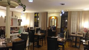 A restaurant with multiple tables and chairs, wooden flooring, and pendant lighting. - Hôtel de la Poste (Pontgibaud)