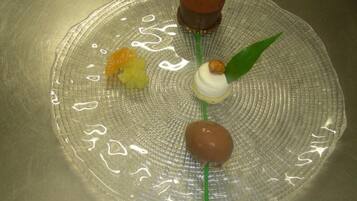 A dessert plate with four items: a chocolate sphere, a white sphere with a green leaf, a yellow fruit, and a brown sphere.