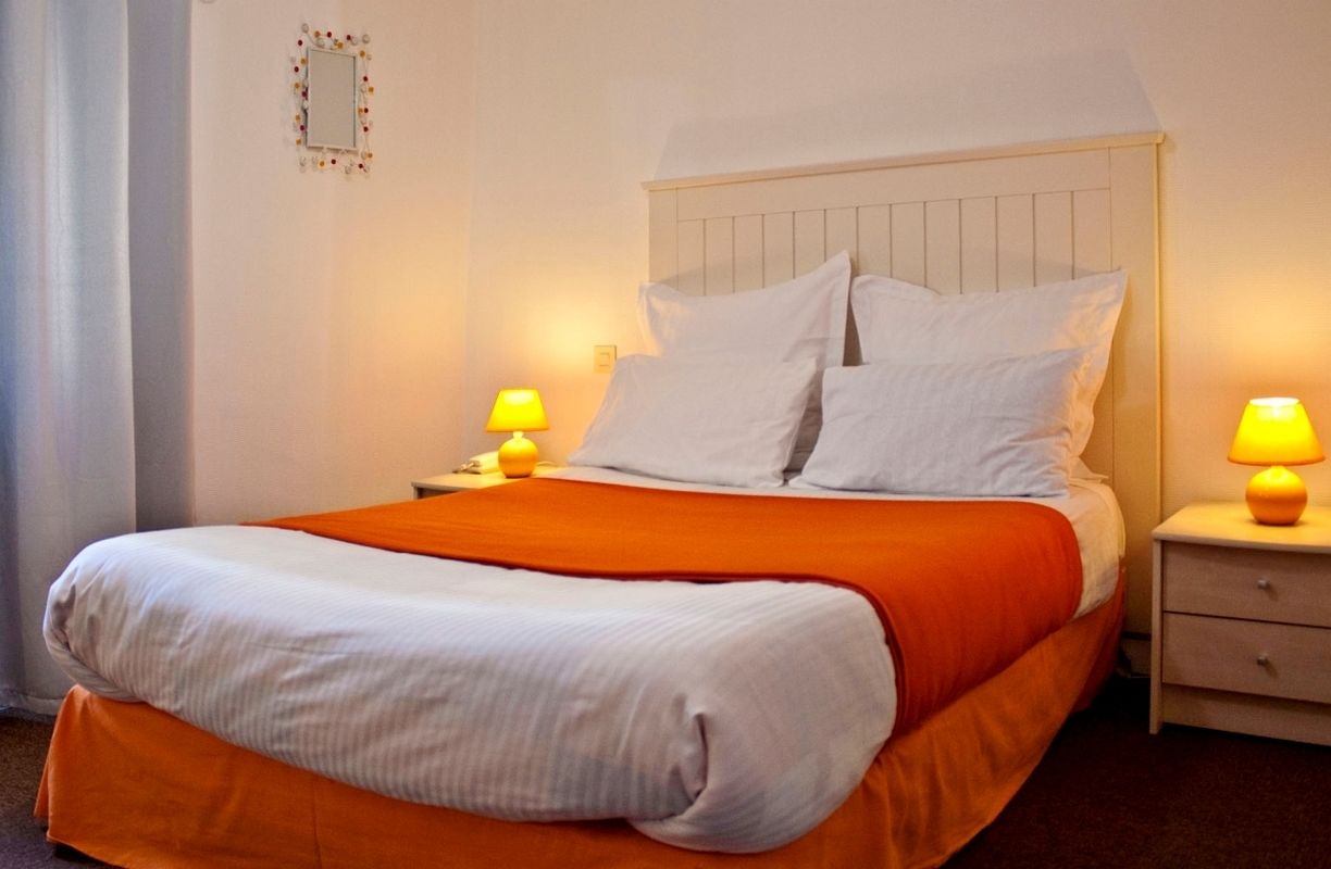 A neatly made bed with white and orange bedding, two bedside lamps, and a small decorative item on the wall.