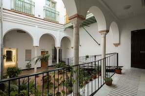 A spacious courtyard with multiple arches, potted plants, and a staircase leading to an upper level.