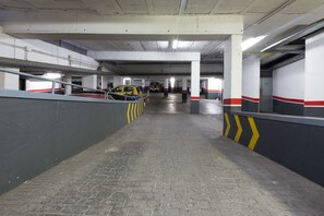 An underground parking garage with concrete pillars, a brick floor, and yellow and red striped barriers.