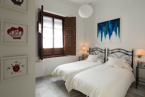 A bedroom with two beds, a window with curtains, a painting, and a radiator.