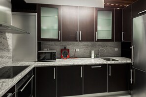 A modern kitchen with dark cabinetry, a stainless steel refrigerator, a built-in microwave, and a granite countertop. - 1 bedroom in Triana, free parking (Sevilla)