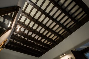 Ein Zimmer mit geneigter Decke, freiliegenden Holzbalken und einem Oberlicht.