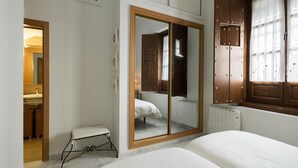 Ein Schlafzimmer mit einem Bett, einem kleinen Hocker, einem Kleiderschrank und einem Fenster mit Vorhängen.