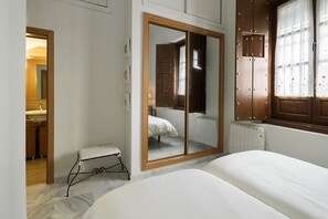 A bedroom with a bed, a small stool, a wardrobe, and a window with curtains.