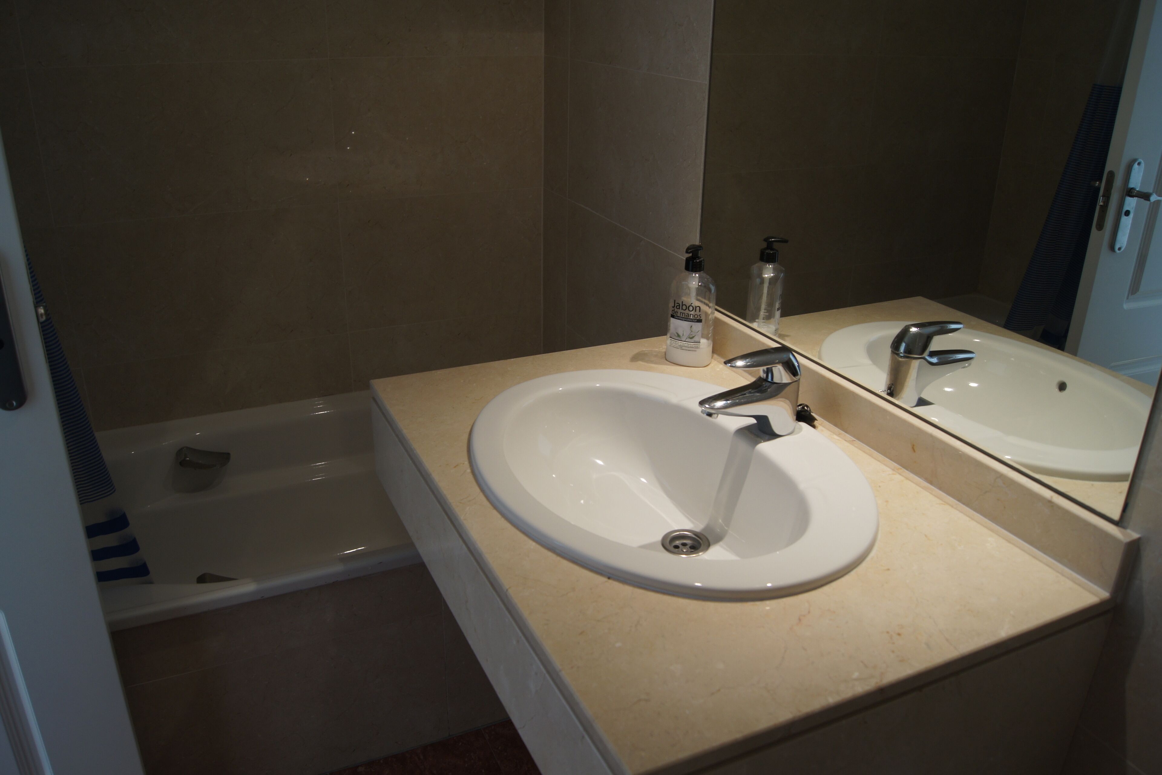 A bathroom with a white sink, a mirror, and a bottle of soap.