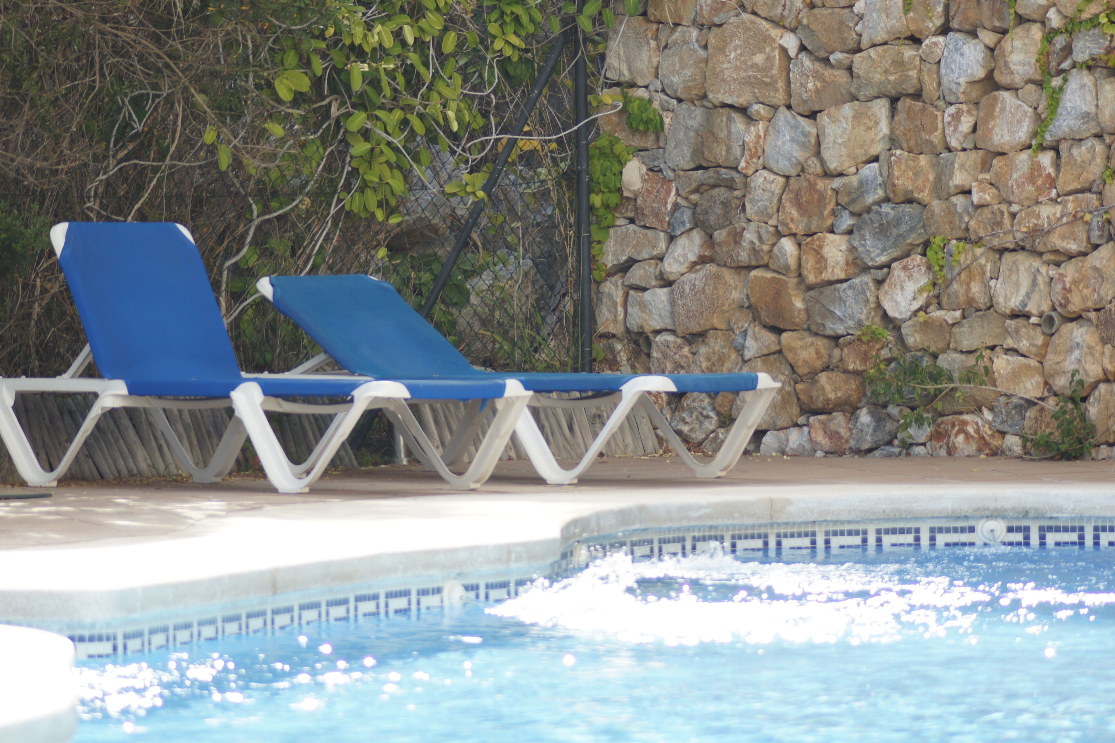 Una piscina con due comode poltrone blu e un muro di pietra sullo sfondo.