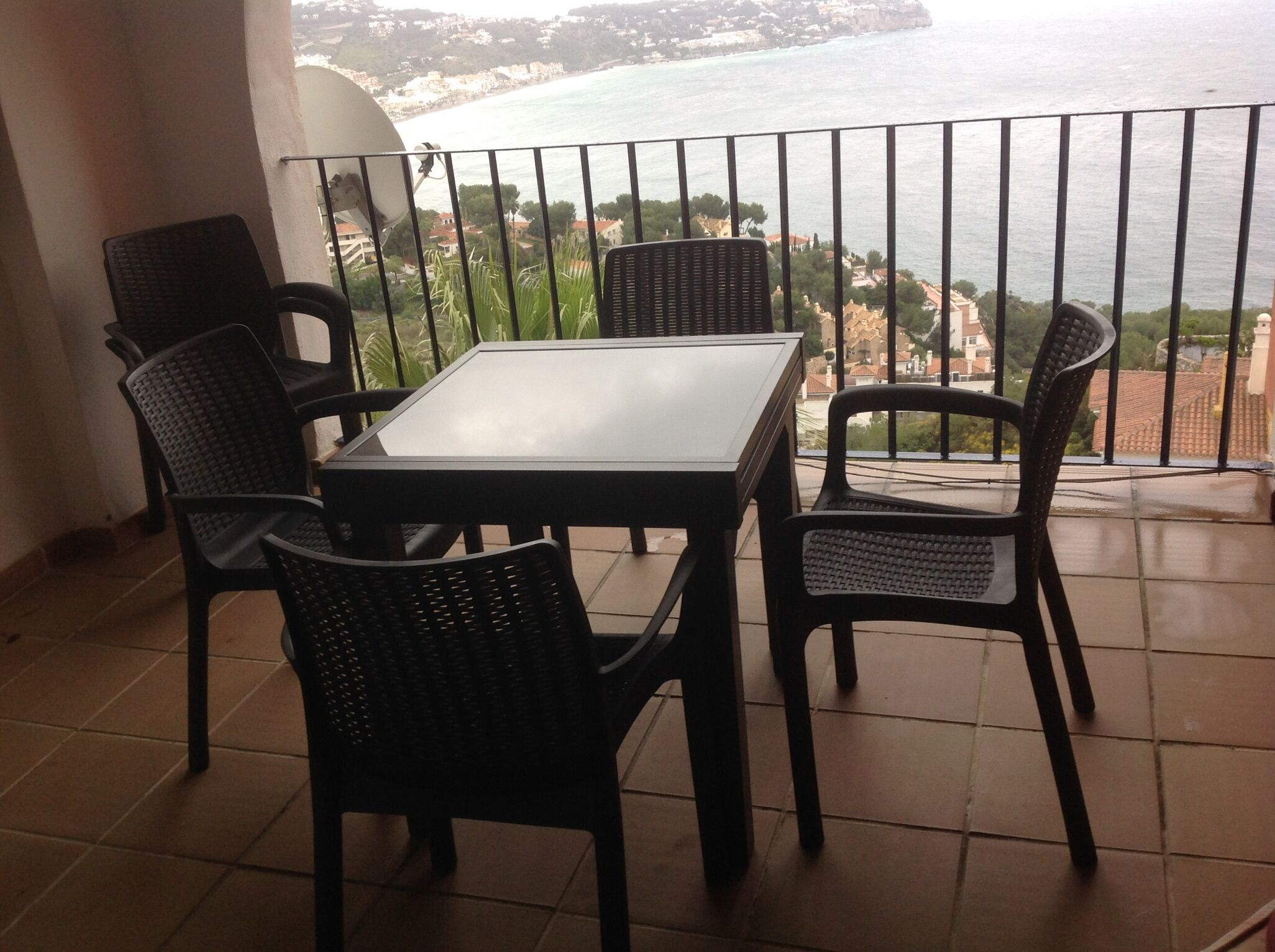 Un balcon avec une table et des chaises, offrant une vue sur la côte, avec des bâtiments et la mer.