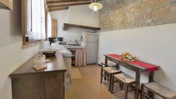 A kitchen with a stone wall, wooden beams, a red tablecloth, and a basket on the counter.