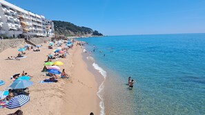 Une plage où des gens se prélassent au soleil et se baignent, un ciel dégagé et un bâtiment doté de balcons.