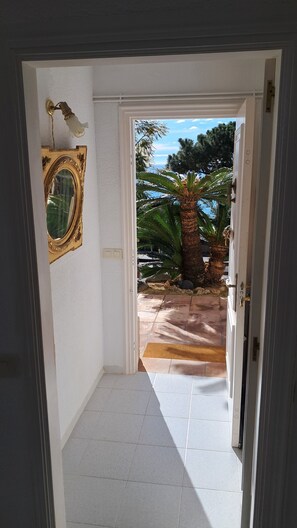 Un couloir qui mène à un patio agrémenté d’un palmier et offrant une vue sur le ciel.