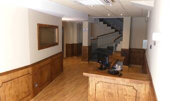 A hotel lobby with wooden paneling, a reception desk, a staircase, and a wall-mounted air conditioning unit.