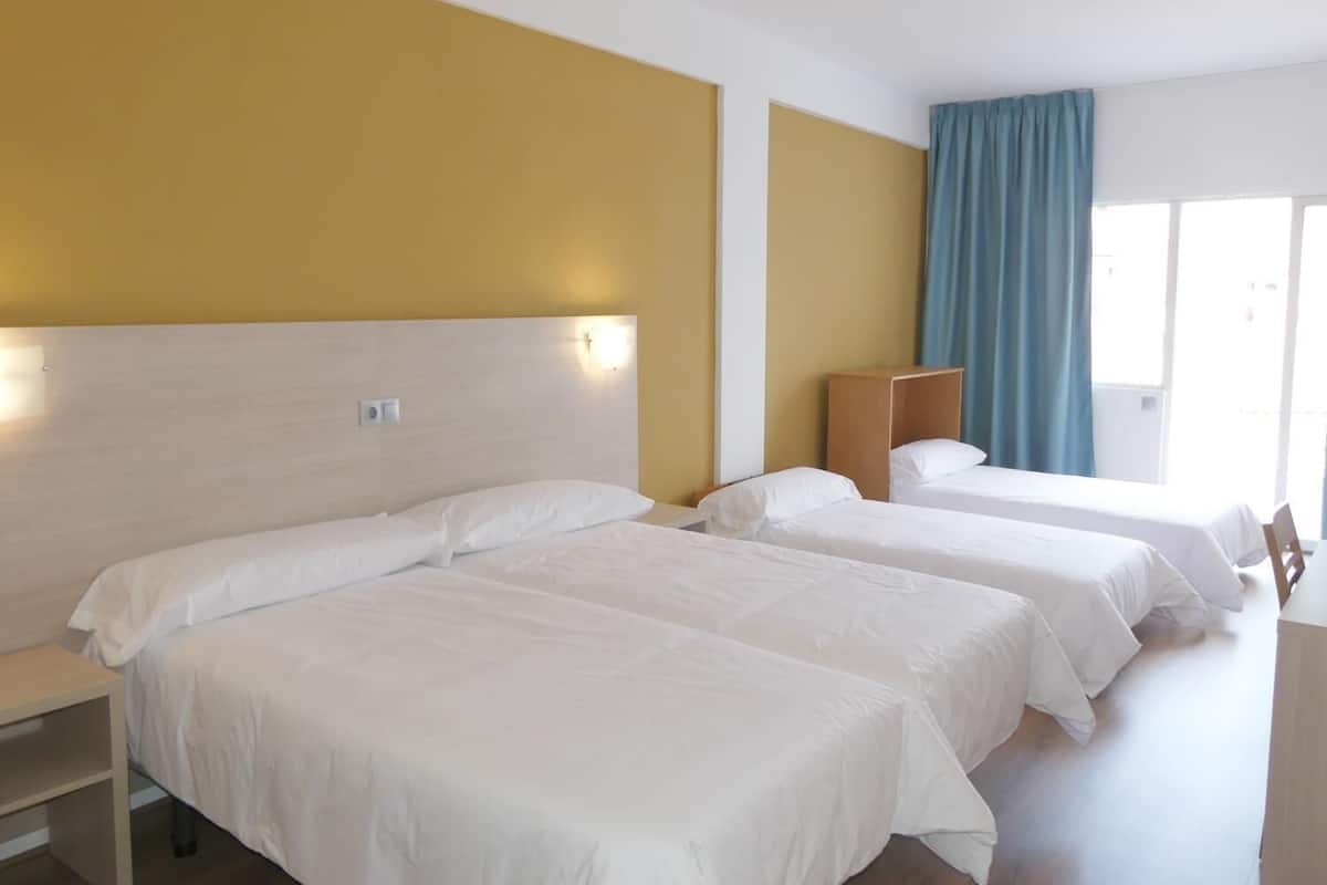 Una habitación de hotel con dos camas individuales, un cabecero de madera, una mesita de noche y una ventana con cortinas azules.