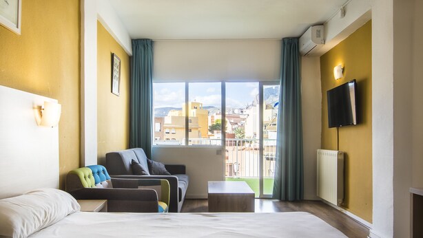 Une chambre d’hôtel avec un grand lit, un canapé, une petite table et un téléviseur fixé au mur.